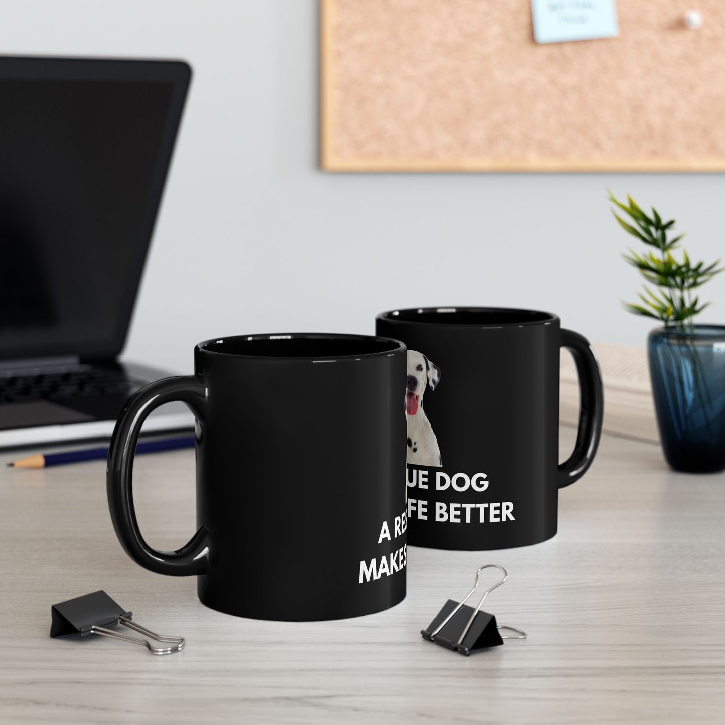 Two black mugs with text on a desk with office supplies and a plant.