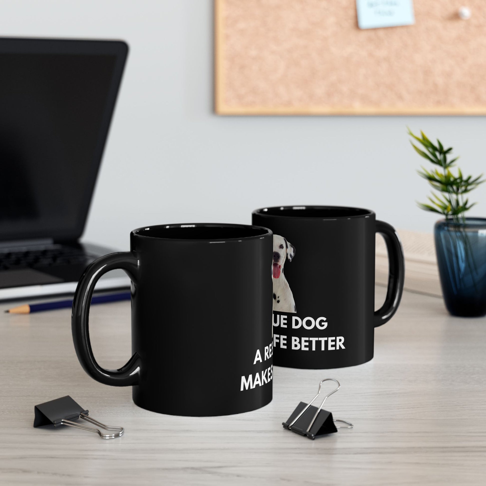 Two black mugs with text on a desk with office supplies and a plant.